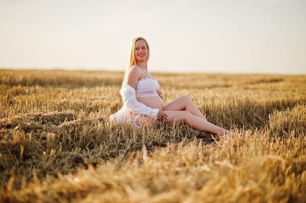 Blondynki kobieta w ciąży w wianku polu przy białą bielizną odziewa na zmierzchu
