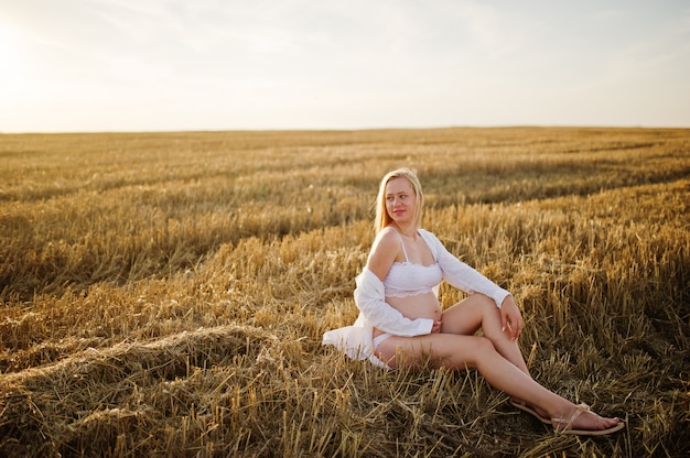 Blondynki kobieta w ciąży w wianku polu przy białą bielizną odziewa na zmierzchu