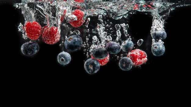 Blueberry i maliny rozpływające się w krystalicznie czystej wodzie z pęcherzami powietrza i tonące