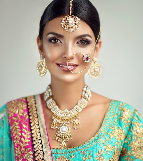 Błyszczące czarne oczy i zębaty uśmiech na twarzy kobiety ubranej w pełny złoty komplet indyjskiej biżuterii