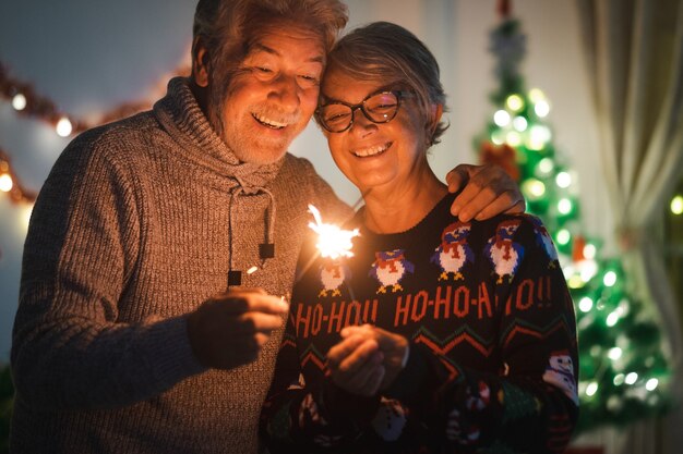 Błyszczące światła i szerokie uśmiechy dla starszej pary dziadków świętujących Boże Narodzenie.