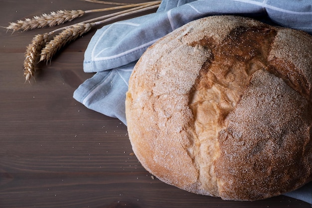 Bochenek świeżo upieczonego domowego chleba rzemieślniczego w lnianej serwetce i kłoskach z ziarnami pszenicy na drewnianej powierzchni Selektywne skupienie