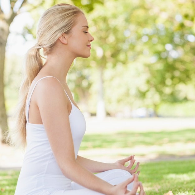 Boczny widok ponytailed spokojna kobieta medytuje siedzieć w parku