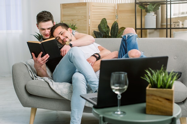 Boczny widok zrelaksowanej młodej homoseksualnej pary czytelnicza książka na leżance w domu