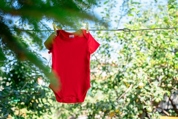 Body niemowlęce dla dziecka wiszą na linie za pomocą spinaczy do bielizny na tle letniego ogrodu.
