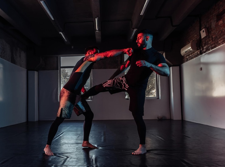 Zdjęcie bojownicy mma ćwiczą kopnięcia i obronę w neonowym świetle w sali sportowej