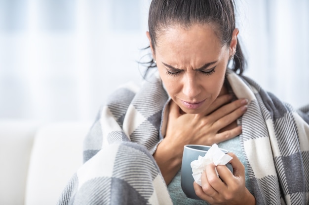 Ból gardła kobiety z przeziębieniem w domu w sezonie grypowym.