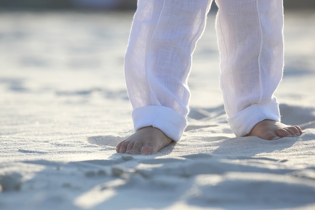 Bose stopy dziecka w białych spodniach na piasku