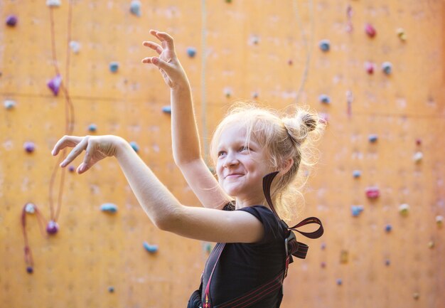 Bouldering, Mała Dziewczynka Wygłupia Się Na Tle ściany Wspinaczkowej