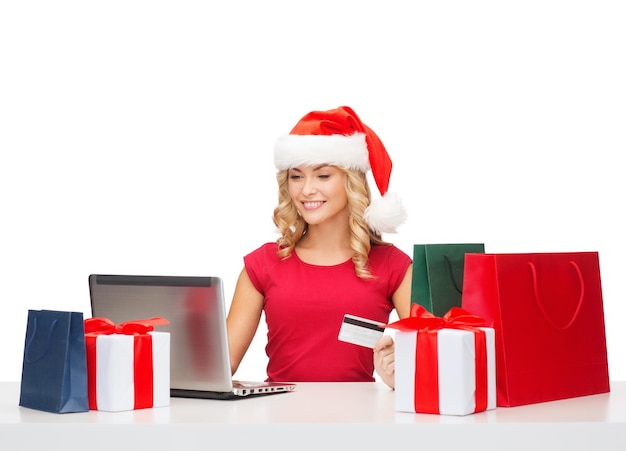 Boże Narodzenie, Boże Narodzenie, koncepcja zakupów online - kobieta w kapeluszu pomocnika Świętego Mikołaja z pudełkami na prezenty, torbami, laptopem i kartą kredytową