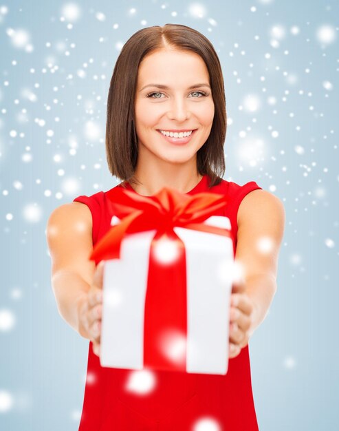 Zdjęcie boże narodzenie, boże narodzenie, walentynki, koncepcja uroczystości - uśmiechnięta kobieta w czerwonej sukience z pudełkiem na prezent