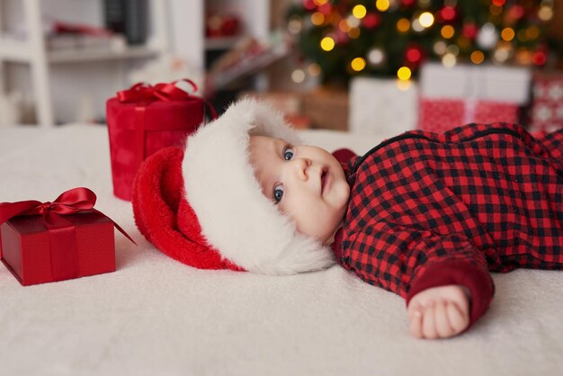 Boże Narodzenie chłopca w santa hat na tle choinki z prezentami.