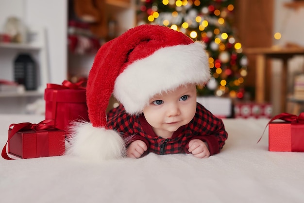 Boże Narodzenie chłopca w santa hat na tle choinki z prezentami.