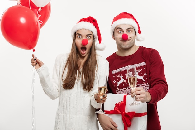 Boże Narodzenie Concept Młoda para Kaukaski trzymająca prezenty szampana i balon robi śmieszną minę na Boże Narodzenie