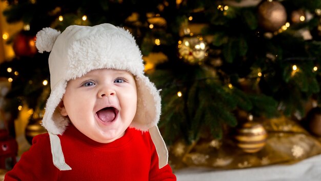 Boże Narodzenie dziecko się uśmiecha. śliczna mała dziewczynka w czerwonej sukience i białym kapeluszu wyraża emocje. Koncepcja Bożego Narodzenia z małym dzieckiem