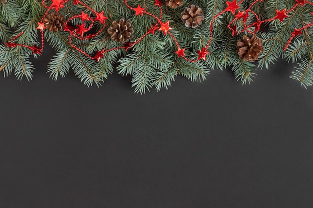 Boże Narodzenie graniczy z gałęziami jodły, szyszkami i czerwoną girlandą na czarnym tle.