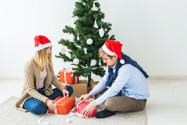 Boże Narodzenie i święta koncepcja - Młoda szczęśliwa para w kapeluszach santa otwieranie prezentów w domu.