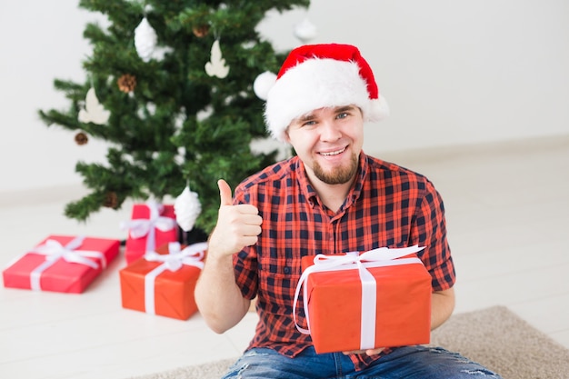 Boże Narodzenie i święta koncepcja - zabawny mężczyzna w santa hat trzyma prezent w domu w salonie