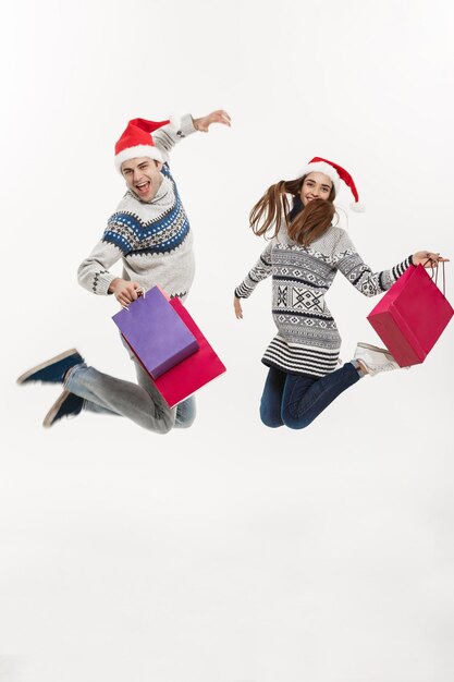 Boże Narodzenie koncepcja pełnej długości Młoda atrakcyjna para trzymająca torby na zakupy i skacząca na białym szarym tle