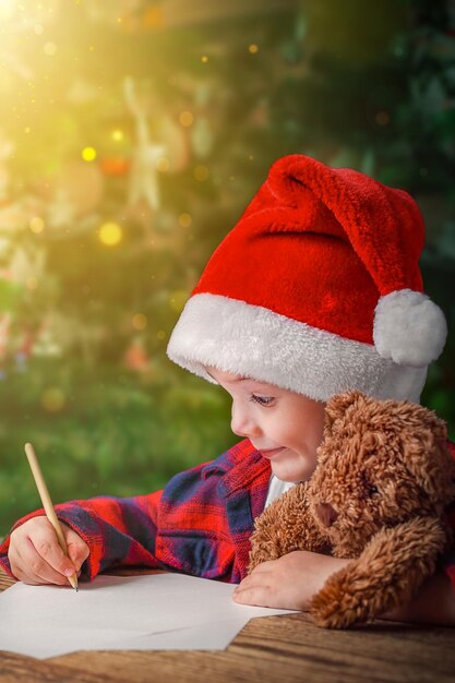 Boże Narodzenie portret dziecka w kapeluszu Świętego Mikołaja z pluszowym niedźwiedziem w rękach