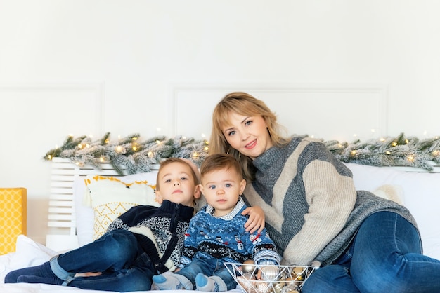 Boże Narodzenie portret matki z jej dwoma synami na łóżku na tle nowego roku. Przytulne wakacje pod jodłą. Miłość, szczęście i wielka koncepcja rodziny. Selektywne skupienie, skopiuj miejsce na górze.