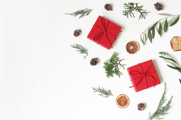 Boże Narodzenie świąteczny wzór kompozycji cyprys oliwny gałęzie szyszki czerwone pudełka na prezenty suche jabłko pomarańczowy owoc na białym tle Zimowy projekt i dekoracja Płaski widok z góry