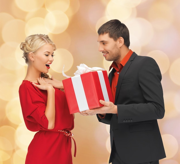 Boże Narodzenie, święta, walentynki, celebracja i koncepcja ludzi - uśmiechnięty mężczyzna i kobieta z prezentem na beżowym tle światła