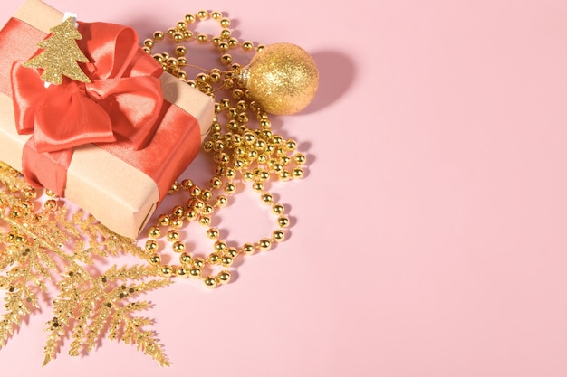 Boże Narodzenie tło z pudełkiem owiniętym papierem pakowym z recyklingu, kokardą z czerwoną wstążką i świąteczną złotą dekoracją.
