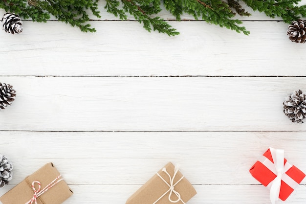 Boże Narodzenie w tle. Choinka wykonana z liści jodłowych, szyszek sosnowych i prezentów prezentuje pudełko z dekoracją elementów rustykalnych na białym drewnie. Kreatywne, płaskie, widok z góry