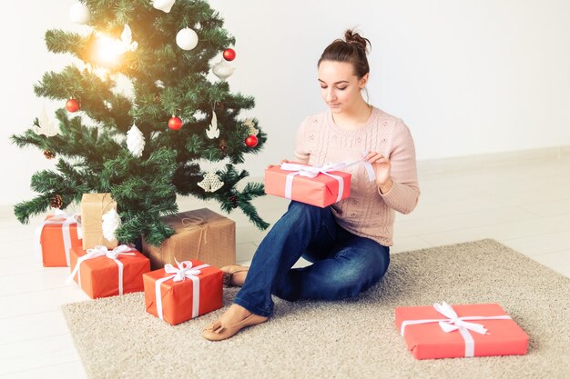 Boże Narodzenie, x-mas, zima, koncepcja szczęścia - dziewczyna otwiera prezent na tle choinki. Szczęśliwa młoda kobieta świętuje Boże Narodzenie
