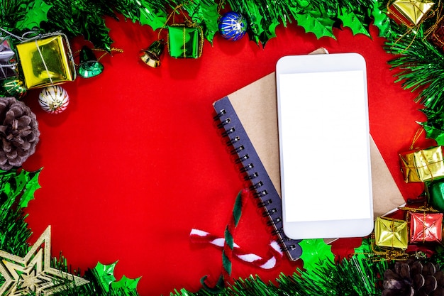 Bożenarodzeniowe świąteczne dekoracje z pustym smartphone, notatnikiem i ołówkiem na czerwień papieru backg ,.
