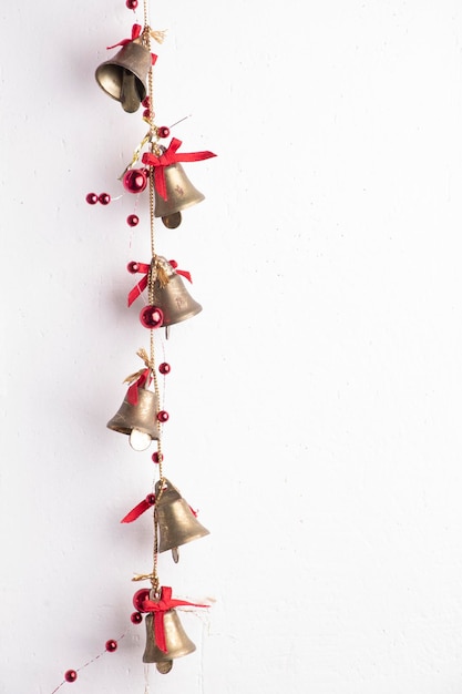 Bożonarodzeniowa ozdoba złotych metalowych dzwonków z czerwonym brokatem bombki z bliska na białej ścianie z teksturą grunge