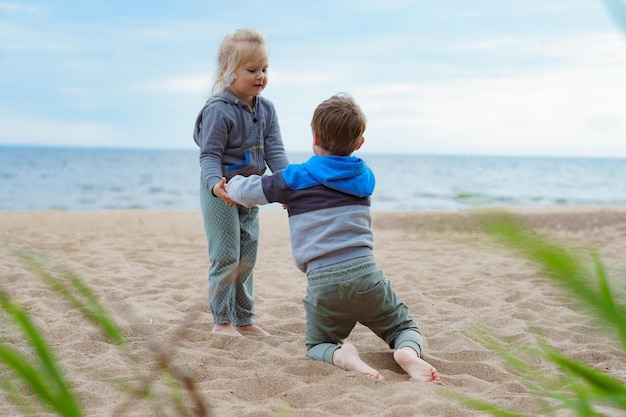 Bracia i młodsza siostra podczas letnich wakacji bawią się na piaszczystej plaży dziewczyna pomaga chłopcu wstać Wsparcie dzieci