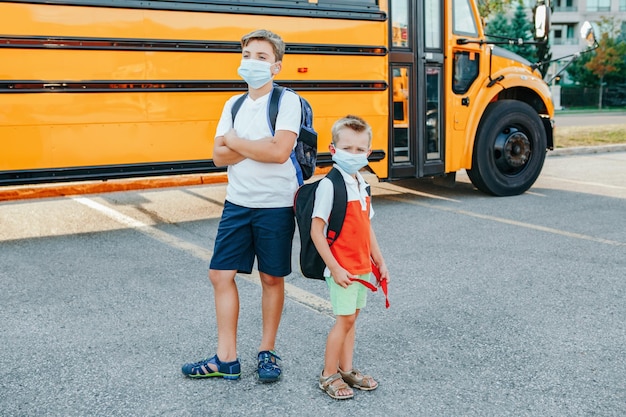 Zdjęcie bracia studenci w maskach stojący przy żółtym autobusie szkolnym na zewnątrz