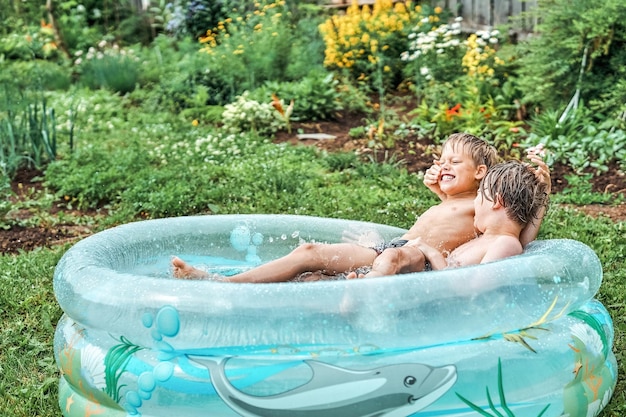 Bracia walczą w nadmuchiwanym basenie dla dzieci na podwórku z bujną zielenią i kwiatami