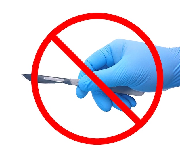 Brak znaku operacyjnego Ręka chirurga w niebieskiej rękawiczce medycznej trzymająca skalpel z czerwonym zakazem izolowanym na białym tle.
