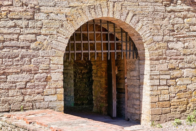 Brama z grubą metalową kratą osłaniającą wejście do twierdzy. Mur z czerwonej cegły z bramami