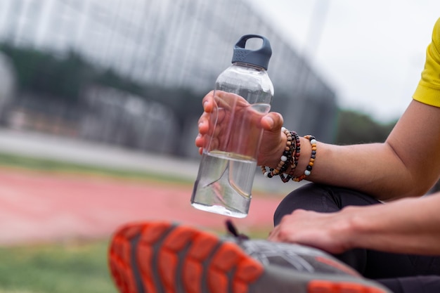 Bransoletki z koralików dla sportowców trzymające plastikową butelkę z wodą odpoczywającą po treningu na arenie sportowej na świeżym powietrzu