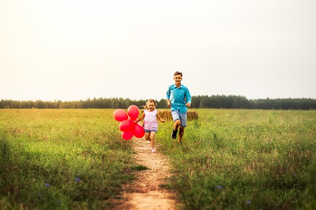 brat i siostra bawią się czerwonymi balonami w lecie w przyrodzie