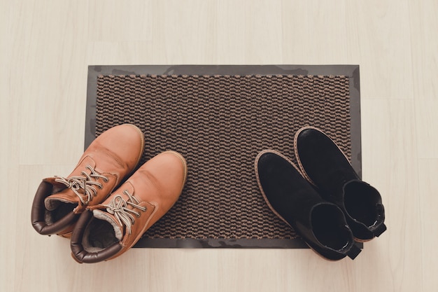 Brązowe damskie zamszowe i czarne buty na czarnym dywanie z napisem powitalnym.