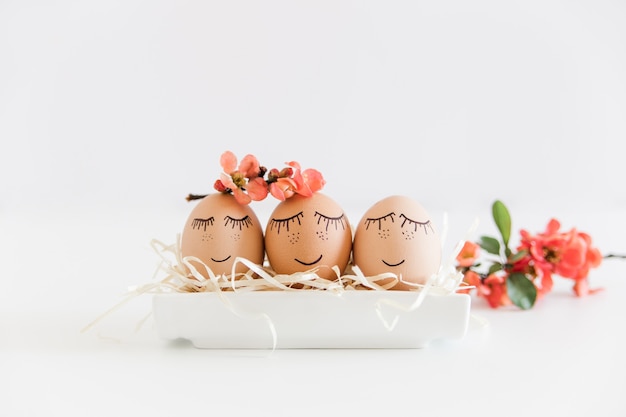 Brązowe ręcznie rysowane jaja z twarzami w gnieździe, z kwitnącymi różowymi kwiatami