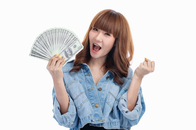 Brązowe włosy Azjatycka kobieta trzyma amerykańskie banknoty, które rozłożone w jej dłoni i wznoszą się podekscytowana pięść, studio strzał na białym tle.