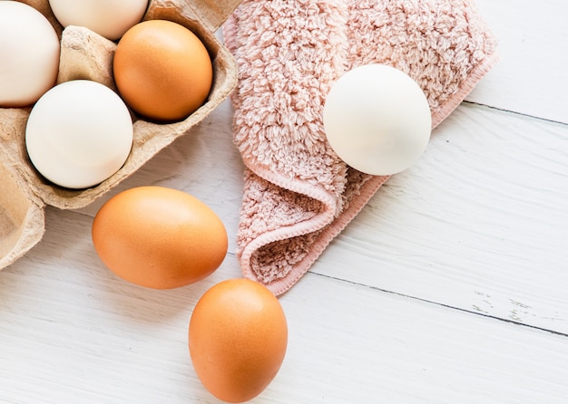 Brązowo-białe organiczne jaja kurze w brązowym papierowym pudełku umieszczonym na białym drewnianym stole. Jajka dostarczają białka, odpowiednie dla miłośników zdrowia. Widok z góry i miejsce na kopię