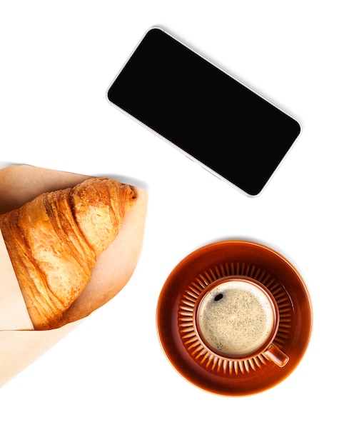 Brązowy kubek czarnej kawy z rogalikiem i telefonem