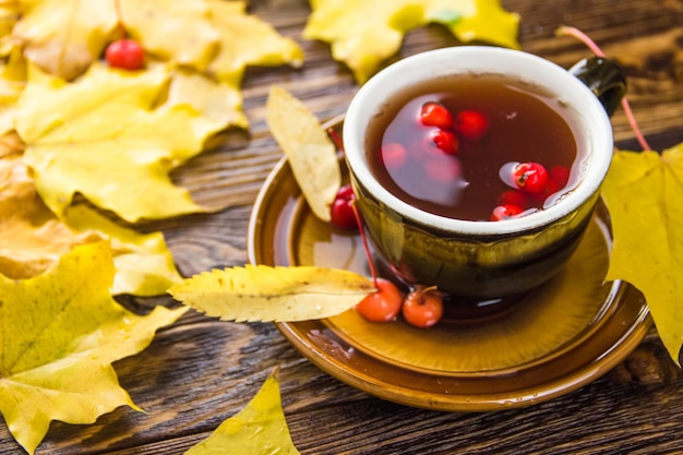 Brązowy kubek herbaty ozdobiony liśćmi jesionu i czerwonymi jagodami