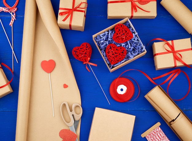 Brązowy papier pakowy, pakowane pudełka na prezenty i przewiązany czerwoną wstążką, czerwone serce, zestaw przedmiotów do robienia prezentów
