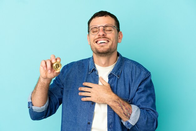 Brazylijczyk trzymający bitcoina na odosobnionym niebieskim tle często się uśmiecha