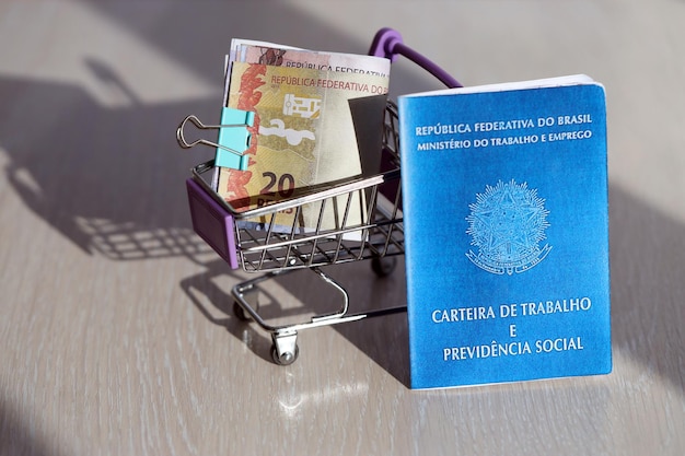 Brazylijska karta pracy i niebieska księga ubezpieczenia społecznego oraz banknoty realów w koszyku zakupowym
