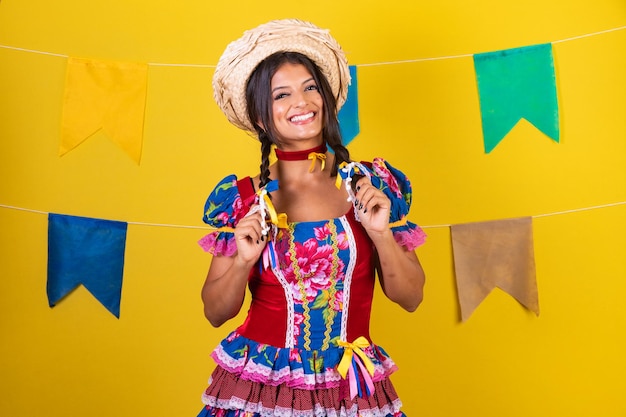 Zdjęcie brazylijska kobieta w ubraniach z festa de sao joao festa junina na żółtym tle z flagami