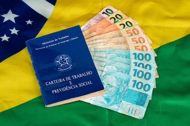 Brazylijska praca dokumentacyjna i ubezpieczenie społeczne Carteira de Trabalho e Previdencia Social z brazylijskimi banknotami pieniężnymi i brazylijską flagą w tle